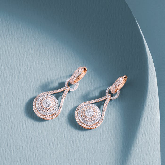 Pair of luxury diamond earrings displayed on a textured blue background.